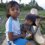 Kinder am Vulkanstrand von Bali beim Aushoehlen einer Kokusnuss